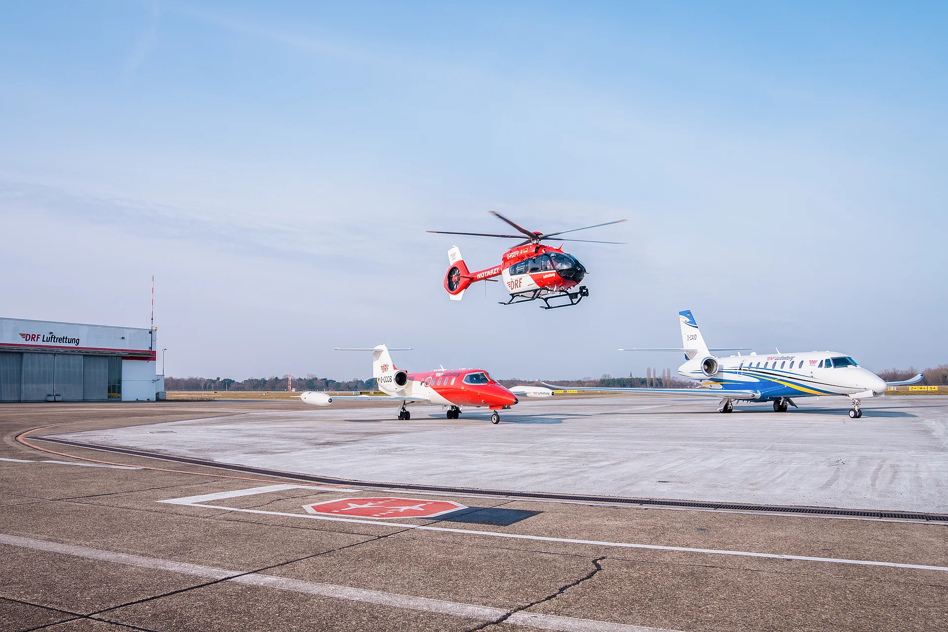 Hubschrauber und Ambulanzflugzeuge der DRF Luftrettung auf dem Vorfeld eines Flughafens